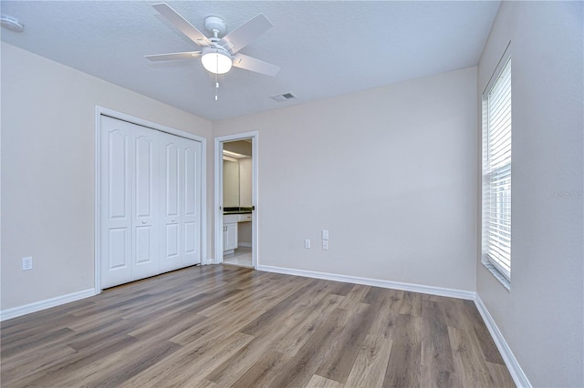 unfurnished bedroom with a closet, light wood-type flooring, multiple windows, and ceiling fan