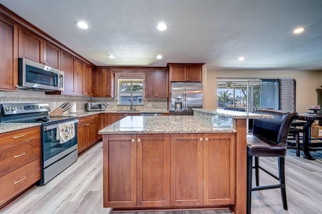 kitchen featuring a kitchen island, appliances with stainless steel finishes, light stone countertops, a breakfast bar, and light hardwood / wood-style flooring