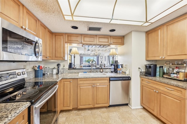 kitchen with sink, stainless steel appliances, light stone counters, a textured ceiling, and light tile patterned floors