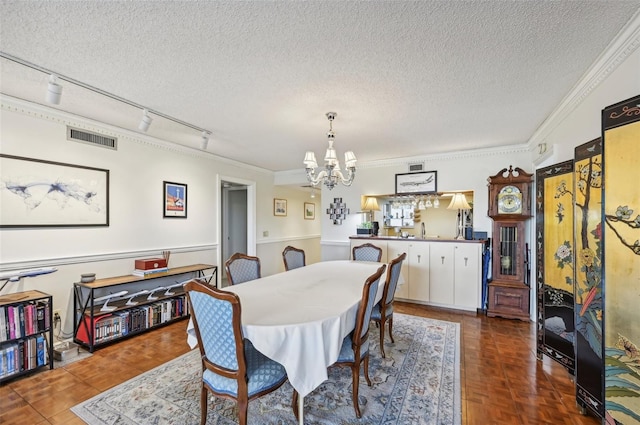 dining room with crown molding, track lighting, a textured ceiling, and an inviting chandelier