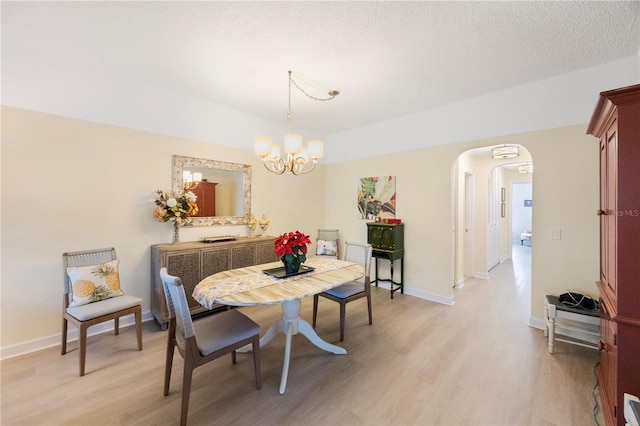 dining area featuring light hardwood / wood-style flooring, a notable chandelier, and a textured ceiling