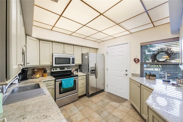 kitchen with light stone countertops, appliances with stainless steel finishes, sink, and cream cabinets