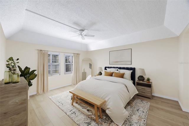 bedroom featuring light hardwood / wood-style floors, ceiling fan, a textured ceiling, and a raised ceiling