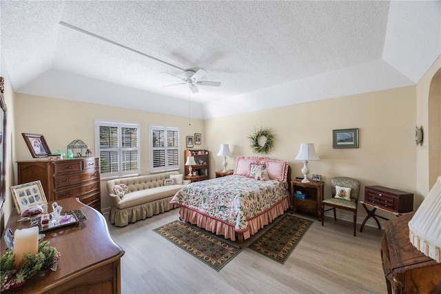 bedroom featuring a textured ceiling, light wood-type flooring, ceiling fan, and a raised ceiling