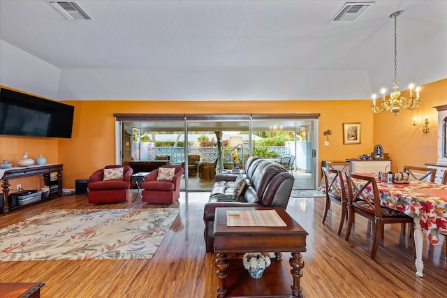 living room with hardwood / wood-style floors, lofted ceiling, a textured ceiling, and a notable chandelier