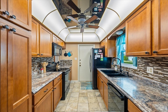 kitchen with sink, tasteful backsplash, dark stone countertops, light tile patterned floors, and black appliances