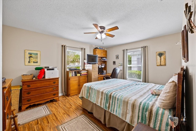 bedroom with multiple windows, ceiling fan, light hardwood / wood-style flooring, and a textured ceiling