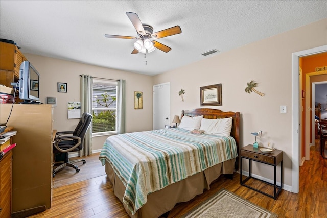 bedroom with ceiling fan, hardwood / wood-style floors, and a textured ceiling