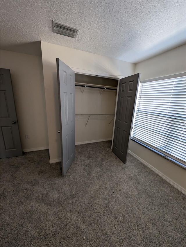 unfurnished bedroom with a closet, a textured ceiling, and dark colored carpet