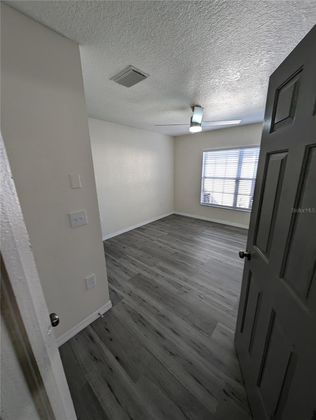 unfurnished room with a textured ceiling, ceiling fan, and dark wood-type flooring