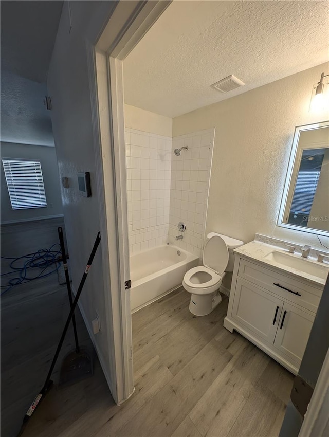 full bathroom featuring vanity, a textured ceiling, wood-type flooring, toilet, and tiled shower / bath