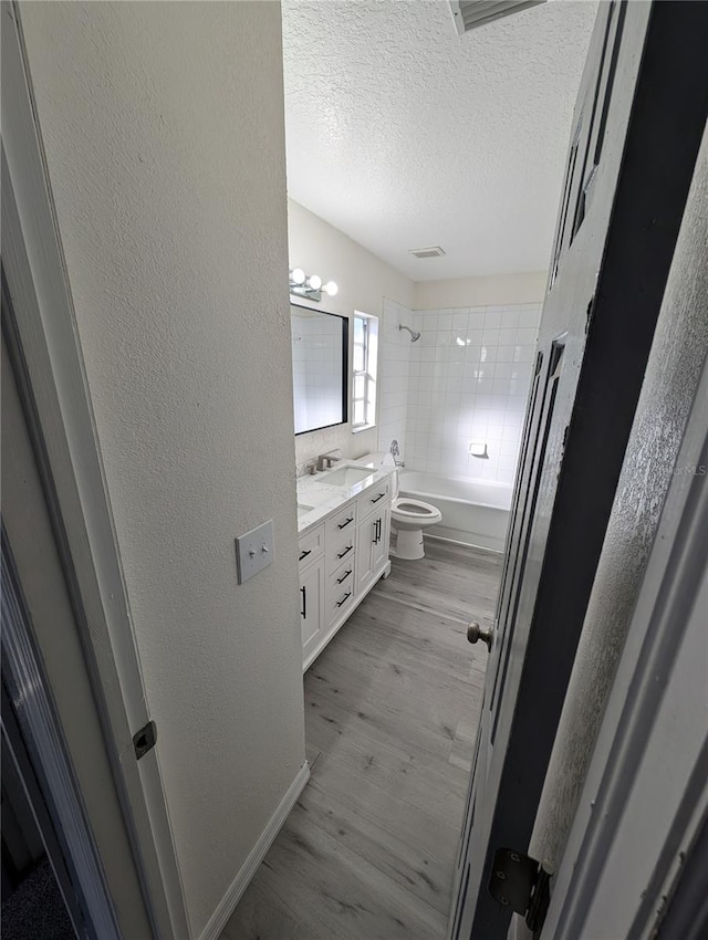 full bathroom featuring vanity, hardwood / wood-style flooring, tiled shower / bath combo, toilet, and a textured ceiling