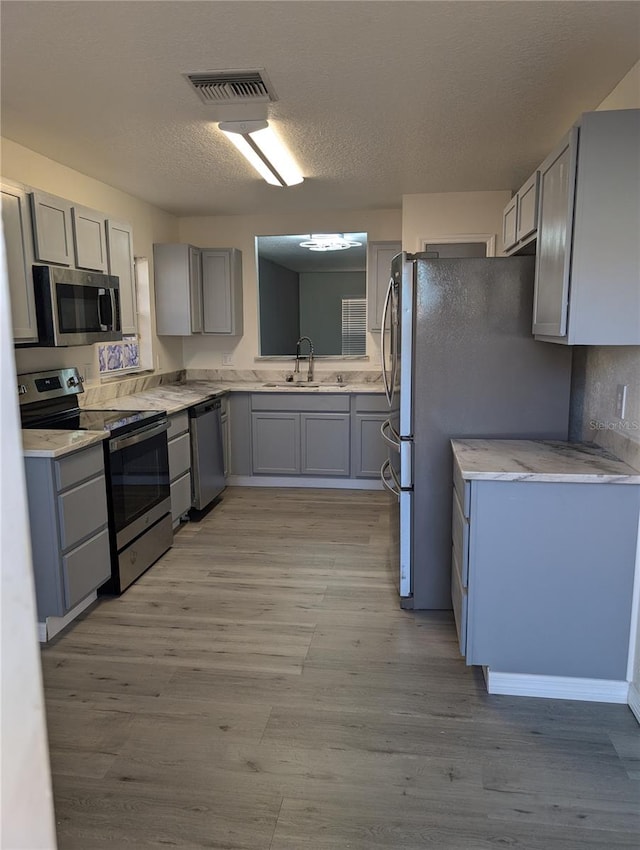 kitchen featuring gray cabinetry, sink, light hardwood / wood-style flooring, a textured ceiling, and appliances with stainless steel finishes