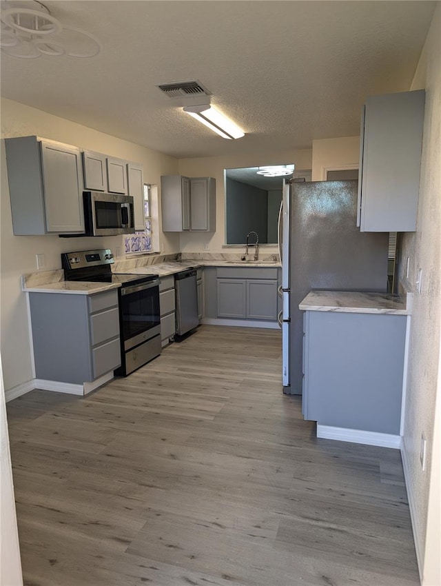 kitchen with appliances with stainless steel finishes, gray cabinetry, a textured ceiling, sink, and light hardwood / wood-style flooring