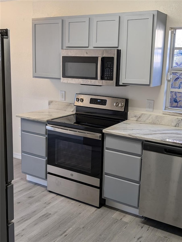 kitchen with light stone countertops, stainless steel appliances, gray cabinets, and light hardwood / wood-style floors