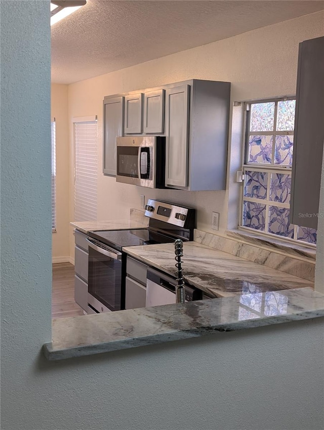 kitchen featuring gray cabinetry, light stone countertops, stainless steel appliances, a textured ceiling, and light wood-type flooring