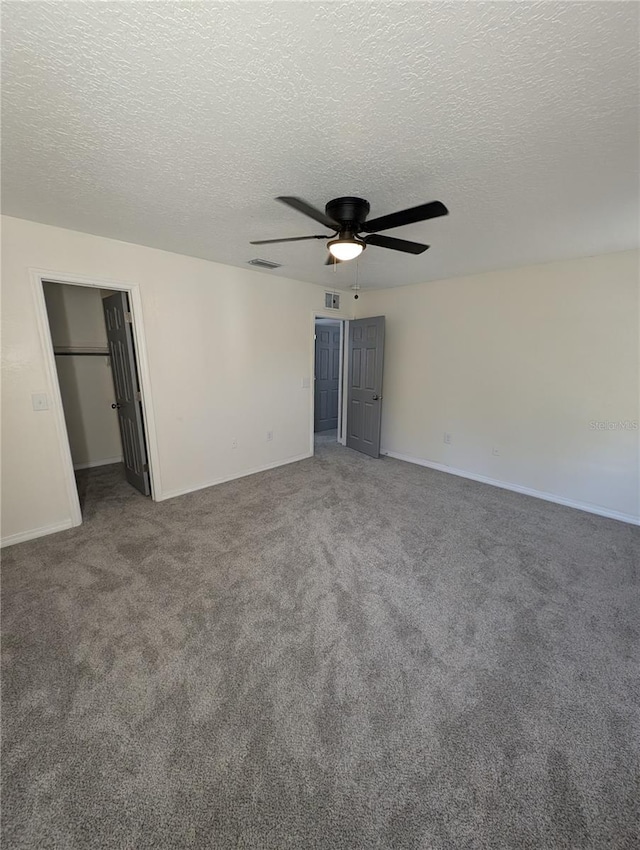 unfurnished bedroom featuring dark colored carpet, a textured ceiling, and ceiling fan