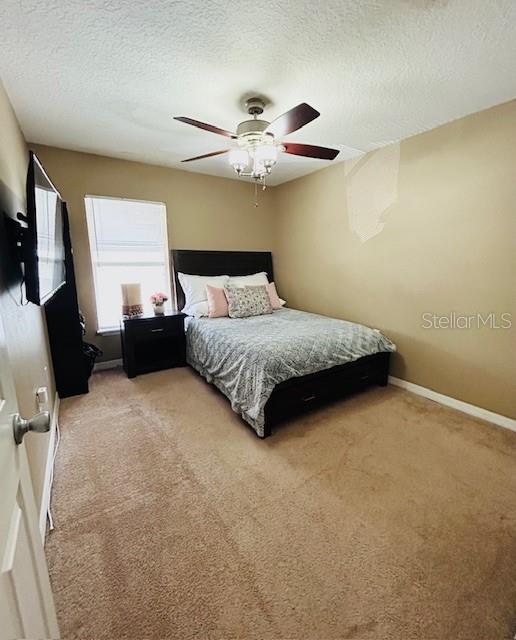 bedroom featuring light carpet, ceiling fan, a textured ceiling, and baseboards