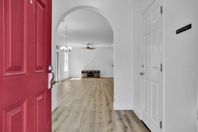 foyer featuring baseboards, arched walkways, light wood-style flooring, and ceiling fan with notable chandelier