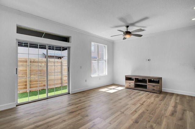 unfurnished living room featuring wood finished floors, baseboards, ceiling fan, a textured ceiling, and crown molding