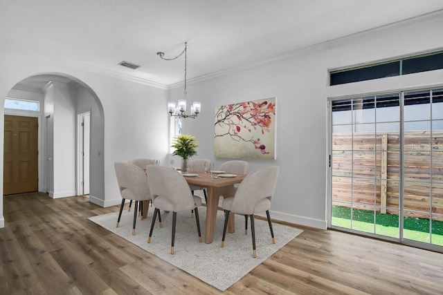 dining space with wood finished floors, visible vents, an inviting chandelier, arched walkways, and ornamental molding