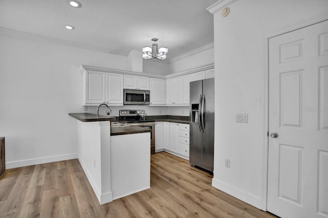 kitchen featuring dark countertops, a peninsula, stainless steel appliances, an inviting chandelier, and white cabinetry