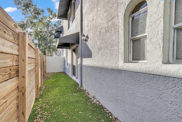 view of side of home with stucco siding and fence