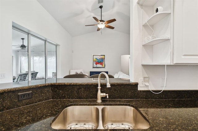 kitchen featuring vaulted ceiling, white cabinetry, sink, dark stone countertops, and ceiling fan