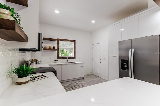 kitchen with stainless steel appliances, light stone countertops, decorative backsplash, sink, and white cabinets