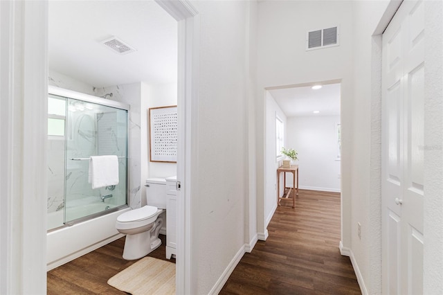 bathroom with hardwood / wood-style floors, shower / bath combination with glass door, and toilet