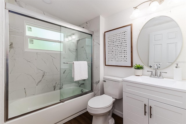 full bathroom featuring hardwood / wood-style floors, combined bath / shower with glass door, vanity, and toilet