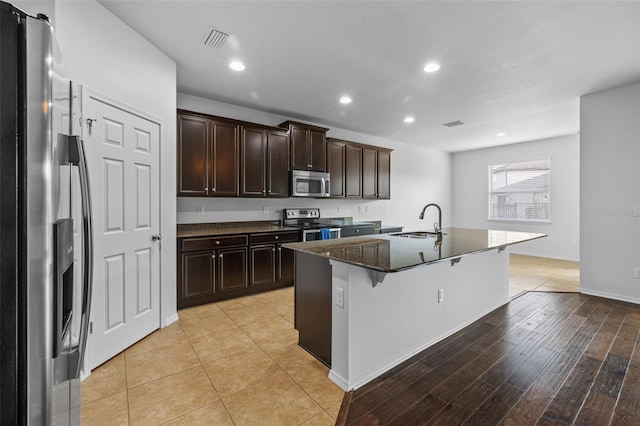 kitchen featuring stainless steel appliances, light hardwood / wood-style floors, sink, a kitchen island with sink, and a kitchen breakfast bar