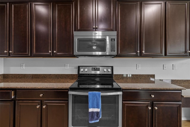 kitchen with dark brown cabinetry, appliances with stainless steel finishes, and dark stone countertops