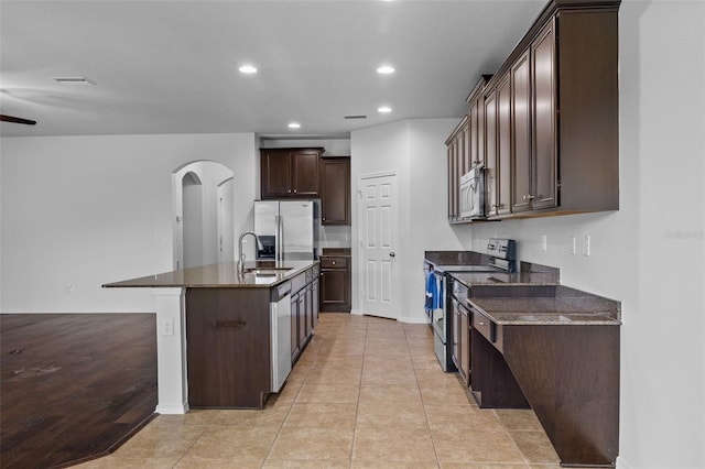 kitchen with stainless steel appliances, dark brown cabinetry, sink, an island with sink, and light tile patterned flooring