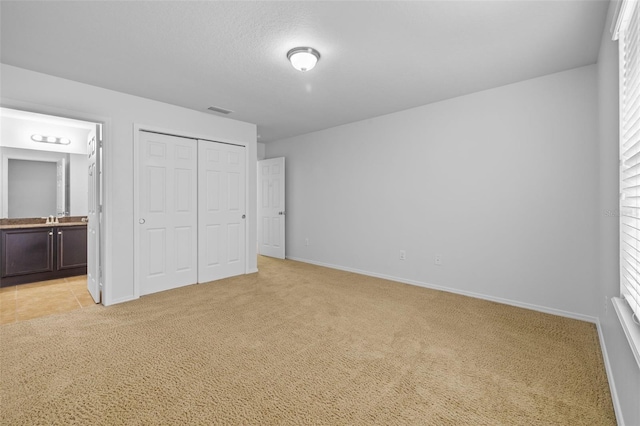 unfurnished bedroom featuring a closet, light carpet, multiple windows, and connected bathroom