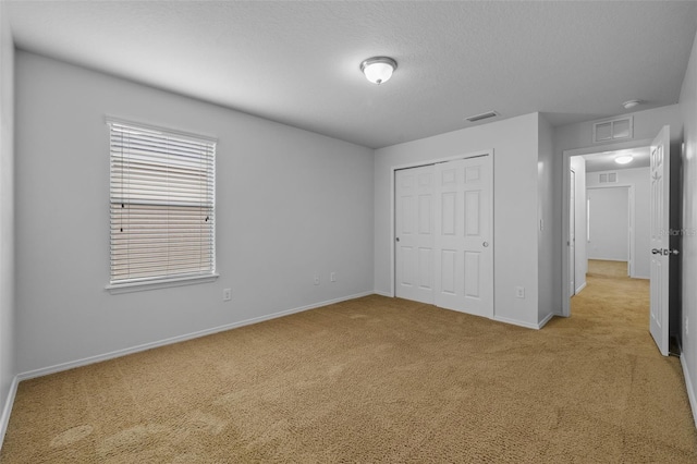 unfurnished bedroom with a closet, a textured ceiling, and light carpet