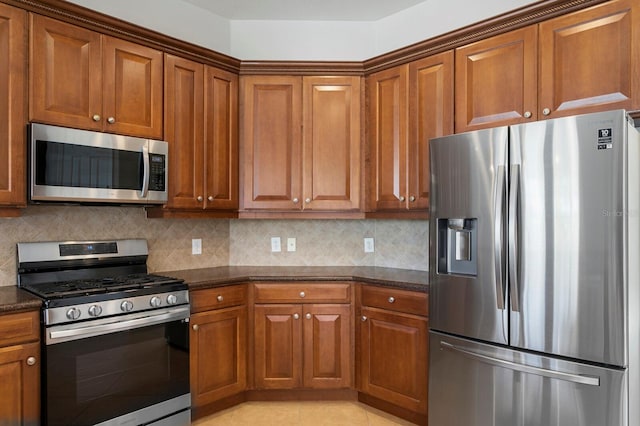 kitchen featuring light tile patterned floors, stainless steel appliances, tasteful backsplash, and dark stone counters