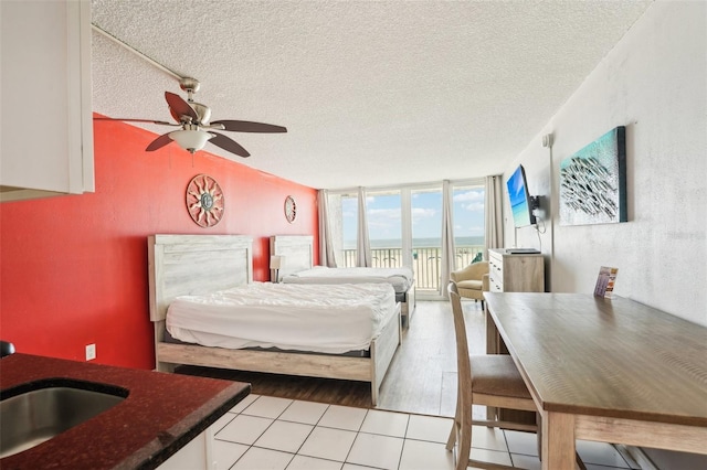 bedroom featuring access to exterior, ceiling fan, sink, light hardwood / wood-style flooring, and a textured ceiling