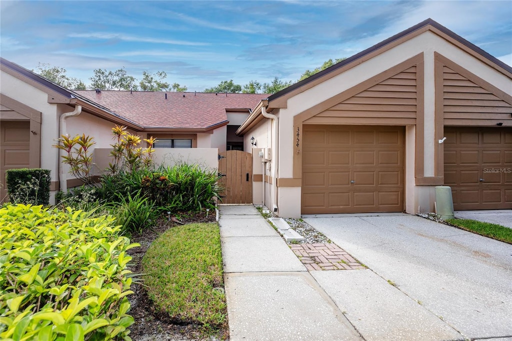 view of front of property with driveway, roof with shingles, an attached garage, a gate, and stucco siding