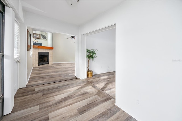 unfurnished living room featuring a ceiling fan, wood finished floors, and a tile fireplace