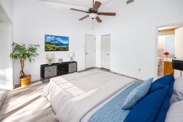 bedroom featuring connected bathroom, visible vents, a towering ceiling, a ceiling fan, and light wood finished floors