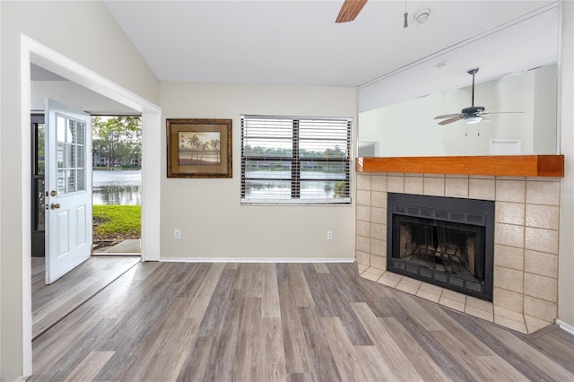 unfurnished living room featuring a tiled fireplace, wood finished floors, a ceiling fan, and baseboards