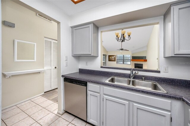 kitchen featuring a tile fireplace, ceiling fan with notable chandelier, a sink, dishwasher, and dark countertops