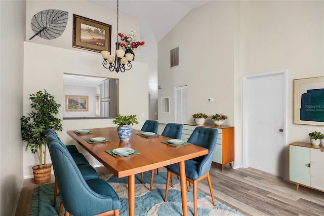 dining area featuring high vaulted ceiling, light wood-style floors, visible vents, and a notable chandelier