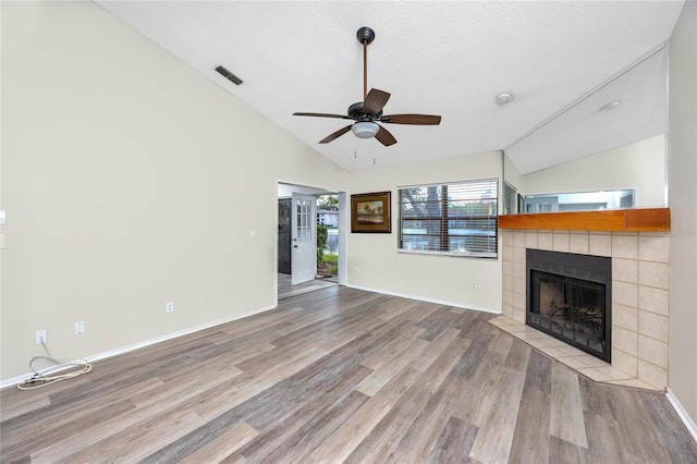 unfurnished living room featuring visible vents, vaulted ceiling, wood finished floors, and a tile fireplace