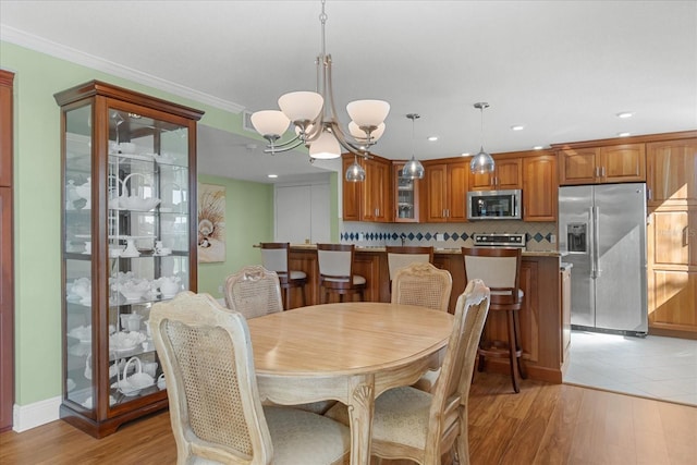 dining space with ornamental molding, a chandelier, and light hardwood / wood-style floors