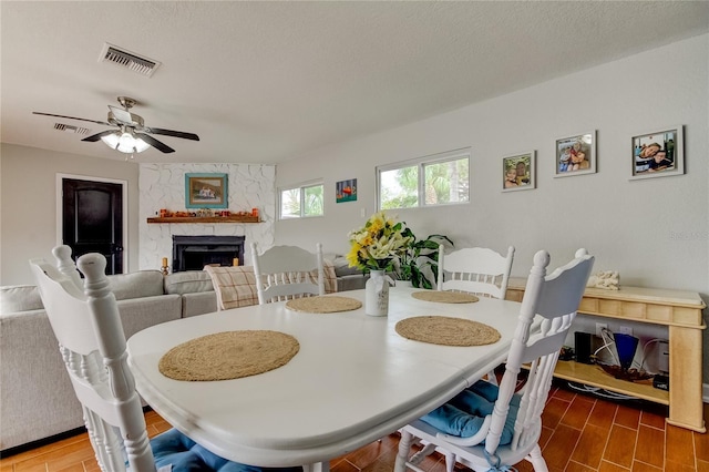 dining area featuring a textured ceiling, a stone fireplace, and ceiling fan