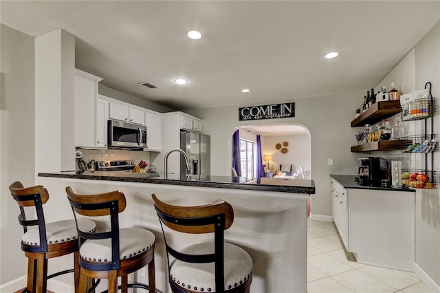 kitchen with kitchen peninsula, decorative backsplash, stainless steel appliances, and white cabinets