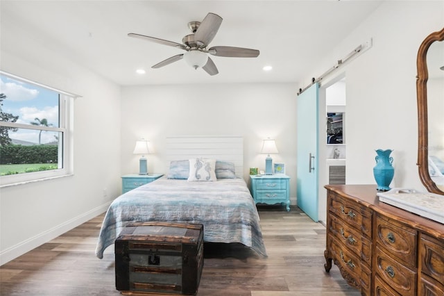 bedroom featuring ceiling fan, a barn door, and dark hardwood / wood-style floors