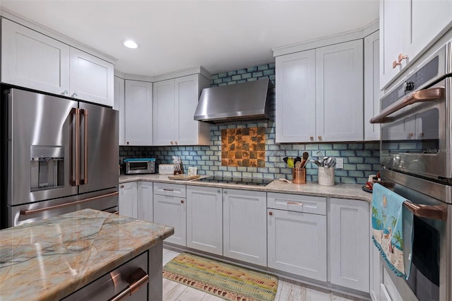 kitchen with stainless steel appliances, wall chimney range hood, light stone countertops, decorative backsplash, and light hardwood / wood-style floors